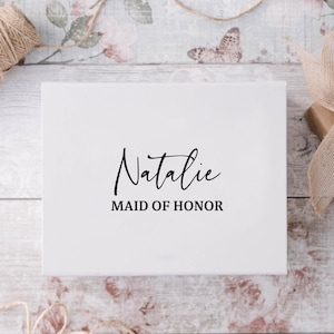 May include: White gift box with black text that reads "Natalie Maid of Honor".