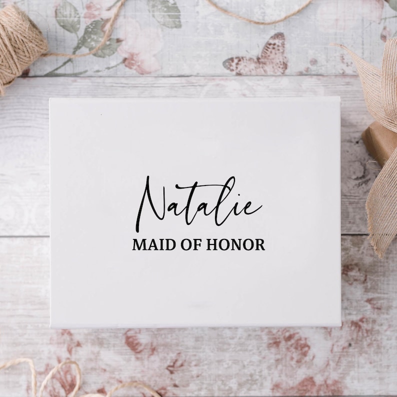 May include: White gift box with black text that reads "Natalie Maid of Honor".