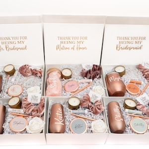 May include: Six white gift boxes with rose gold lids, each containing a rose gold tumbler, a candle, a hair tie, and other small gifts. The boxes are labeled with the text "Thank you for being my..." followed by "Jr Bridesmaid", "Matron of Honor", or "Bridesmaid".