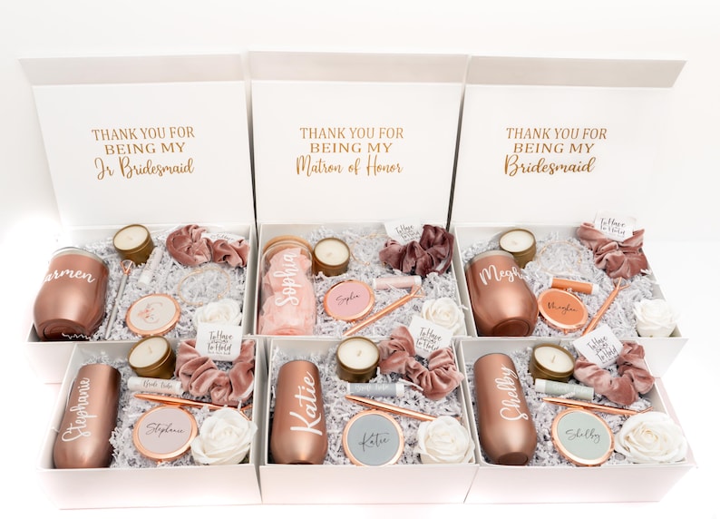 May include: Six white gift boxes with rose gold lids, each containing a rose gold tumbler, a candle, a hair tie, and other small gifts. The boxes are labeled with the text "Thank you for being my..." followed by "Jr Bridesmaid", "Matron of Honor", or "Bridesmaid".