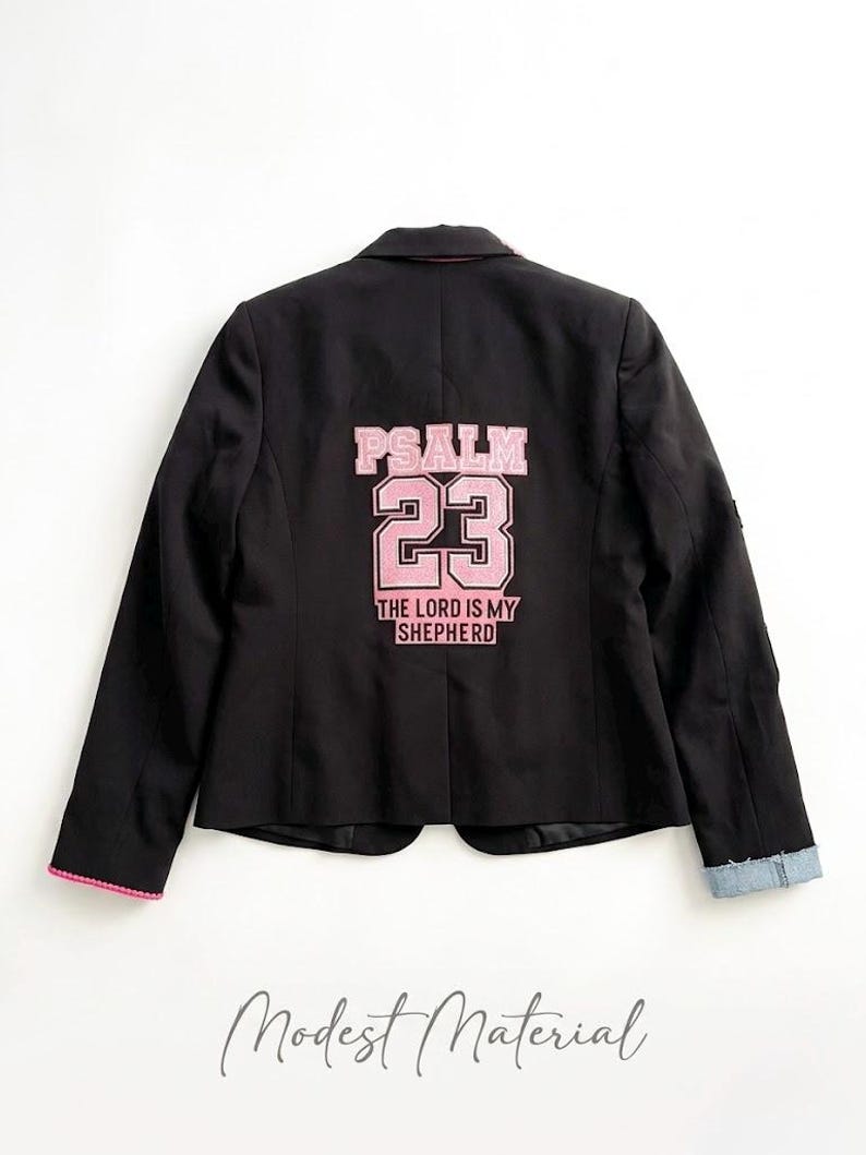 Puede incluir: Blazer negro con ribete rosa y pu&ntilde;o de mezclilla. La parte trasera del blazer presenta el texto "PSALM 23 THE LORD IS MY SHEPHERD" en letras rosas. El blazer es de estilo cl&aacute;sico con un corte entallado.