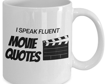 May include: White ceramic coffee mug with black text that reads "I speak fluent movie quotes" and a black and white illustration of a clapperboard.