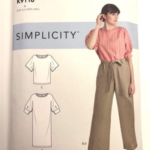May include: A Simplicity sewing pattern envelope K9116 for sizes XXS-XXL. The front displays a photograph of a person wearing a coral striped top with puff sleeves and tan wide-leg trousers with a tie waist, alongside line drawings of the garments.