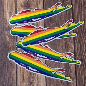May include: Five rainbow-colored Long Island outline stickers on a wood background. The stickers are arranged in a stack, with the top sticker being the most visible. The stickers are made of vinyl and are waterproof and durable.