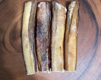 May include: Four cylindrical, dried, light brown and dark brown pet chews arranged vertically. Each chew has a firm, textured, and slightly translucent appearance with varying shades of tan, amber, and deep brown throughout the surface.