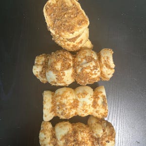 May include: An overhead shot of four pieces of baked goods. The pieces are light brown with a dusting of darker brown crumbs on top. The baked goods are arranged in a vertical line on a dark surface.