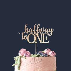 May include: Gold glitter cake topper with the text "halfway to ONE" for a first birthday party.