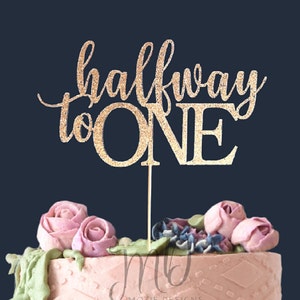 May include: Gold glitter cake topper with the text "halfway to one" for a half birthday celebration.