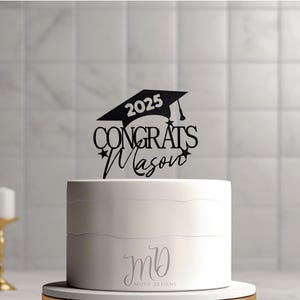Può includere: Topper per torta nero a forma di cappello di laurea con il testo "2025 Congrats Mason" e stelle. Il topper è su una torta bianca con il testo "MD Motif Designs" in basso.