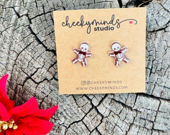 May include: A pair of brown skeleton earrings with a white bow tie. The earrings are on a card that says "cheeky minds studio" and has a social media handle and website address.