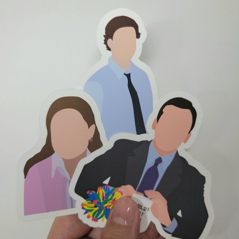 May include: Three illustrated stickers of characters from the TV show "The Office". The stickers are white with black outlines and feature a man in a blue shirt and black tie, a woman in a pink shirt, and a man in a black suit and blue tie. The man in the suit is holding a mug with the text "World's Best Boss" on it.
