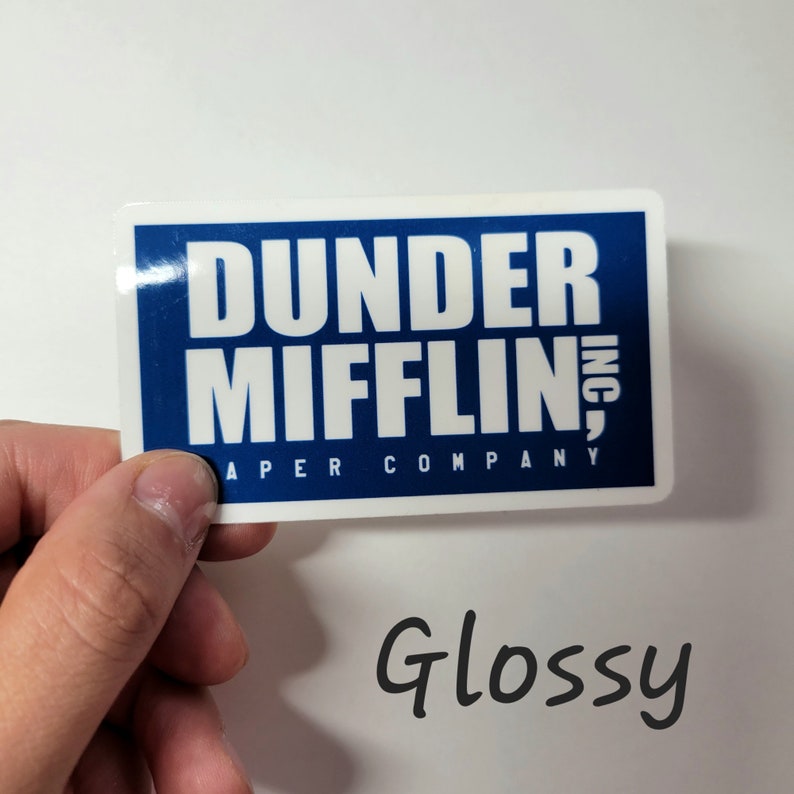 May include: Glossy sticker with the text "Dunder Mifflin, Inc. A Paper Company" in white letters on a blue background.