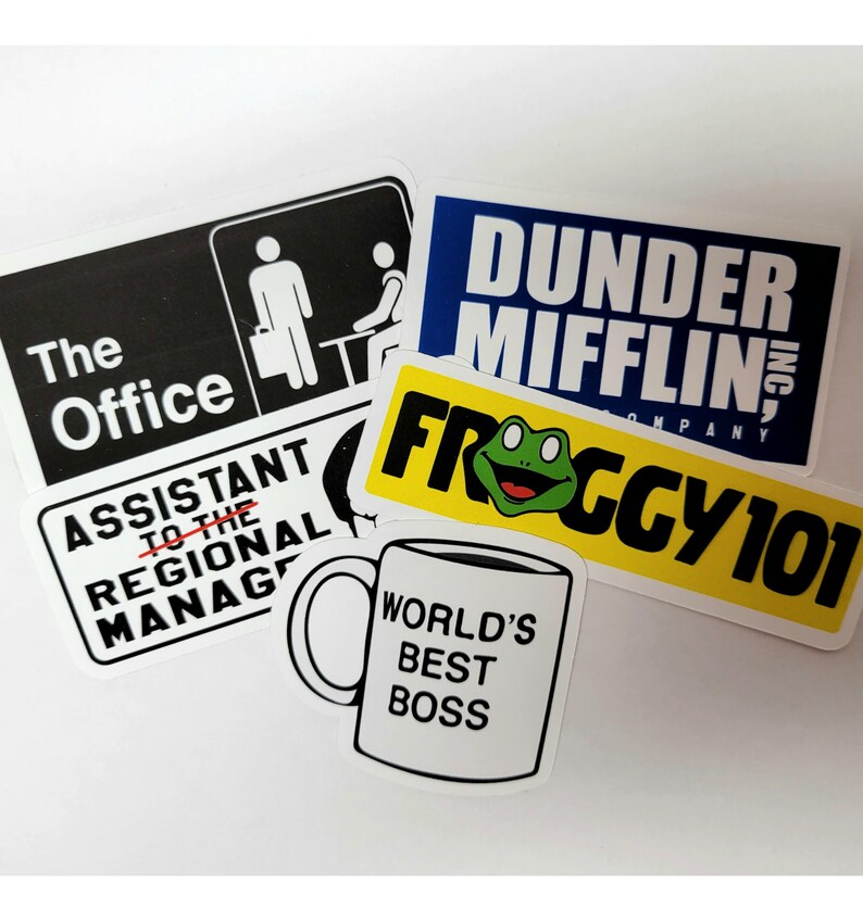 May include: A set of five stickers featuring the popular television show "The Office". The stickers include the office logo, the assistant to the regional manager title, the Dunder Mifflin logo, a frog with the text "Froggy 101", and a coffee mug with the text "World's Best Boss".
