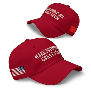 May include: Two red baseball caps with white text that reads "MAKE FRIENDSHIP GREAT AGAIN." One cap has a Chinese flag patch, the other has an American flag patch. The caps are angled, showcasing the text and patches.