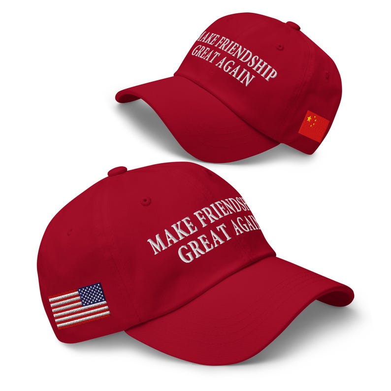 May include: Two red baseball caps with white text that reads "MAKE FRIENDSHIP GREAT AGAIN." One cap has a Chinese flag patch, the other has an American flag patch. The caps are angled, showcasing the text and patches.