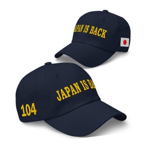 以下が含まれることがあります： 2つのネイビーブルーの野球帽。1つの帽子には、前面に黄色の文字で「JAPAN IS BACK」と書かれており、側面に日本の国旗のパッチが付いています。もう1つの帽子には、前面に黄色の文字で「JAPAN IS BACK」と書かれており、側面に黄色の数字で「104」と書かれています。