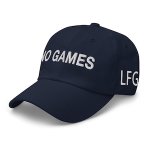May include: A navy blue baseball cap with the words "NO GAMES" embroidered in white across the front. The letters "LFG" are embroidered in white on the side. The cap has a curved peak.