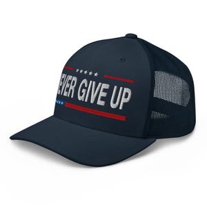 May include: Navy blue trucker hat with the text "NEVER GIVE UP" in white, with red and blue accents. The hat has a mesh back and a curved brim.