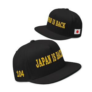 Könnte beinhalten: Zwei schwarze Baseballcaps mit flachem Schirm. Auf der Vorderseite ist in gelber Schrift "JAPAN IS BACK" gestickt. Auf einer Kappe ist die Zahl "104" aufgestickt. Auf einer Kappe befindet sich ein japanischer Flaggenaufnäher.