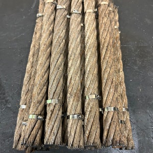 May include: A bundle of thick, braided steel cables, each secured with metal clamps. The cables have a weathered, metallic appearance, with visible strands and a slightly rough texture. The arrangement suggests industrial or construction materials.