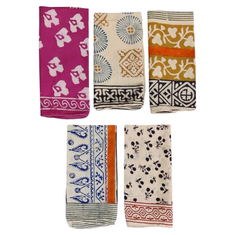 May include: Five folded fabric napkins with various patterns. One is fuchsia with white floral shapes, another is cream with blue circles and brown squares, and a third is yellow with orange and black designs. The other two are cream with black floral and blue patterns.