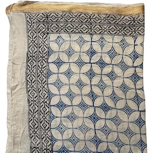 May include: A white cotton scarf with a blue and black geometric pattern. The scarf has a gold trim around the edges.