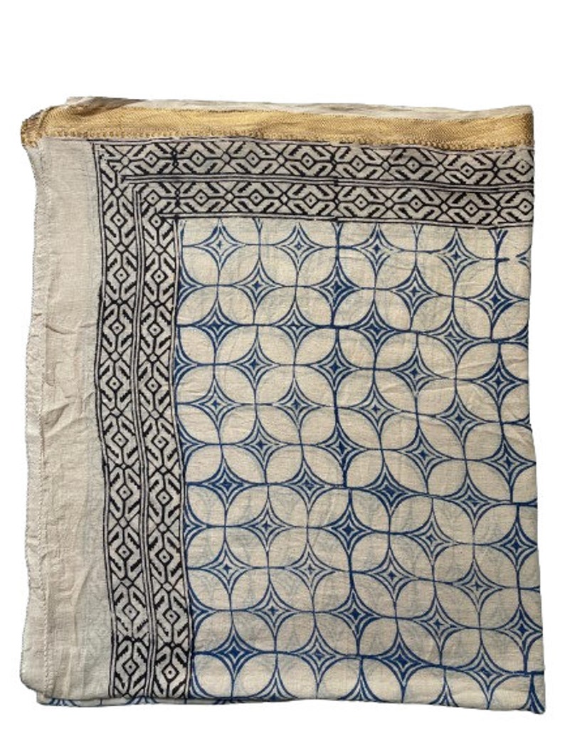 May include: A white cotton scarf with a blue and black geometric pattern. The scarf has a gold trim around the edges.