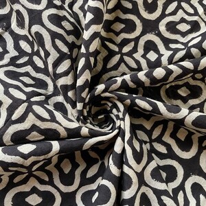 May include: Black and white fabric with a repeating geometric pattern. The fabric is folded and twisted, showing the pattern from different angles.