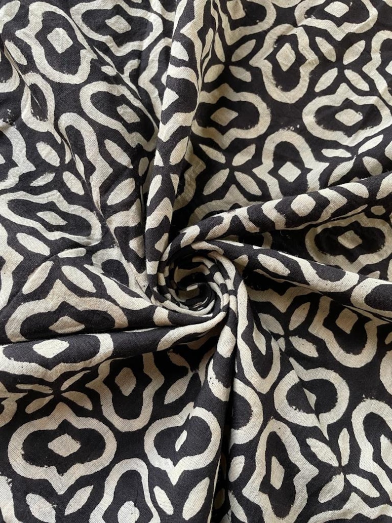 May include: Black and white fabric with a repeating geometric pattern. The fabric is folded and twisted, showing the pattern from different angles.