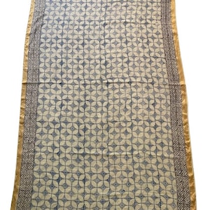 May include: A white cotton fabric tablecloth with a blue and white geometric pattern. The tablecloth has a gold and brown border.