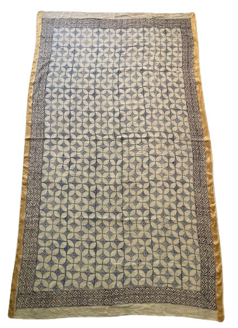May include: A white cotton fabric tablecloth with a blue and white geometric pattern. The tablecloth has a gold and brown border.