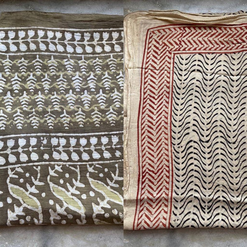 May include: Two folded textiles with printed patterns. One is olive green with white and light green leaf and floral designs. The other is off-white with a red zigzag border and black wavy lines. The fabrics appear to be lightweight.