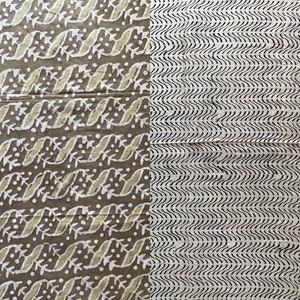 May include: A textile with two distinct patterns. One side features a repeating design of white leaves and dots on a brown background. The other side has black wavy lines on a cream background. The fabric appears to be cotton or linen.