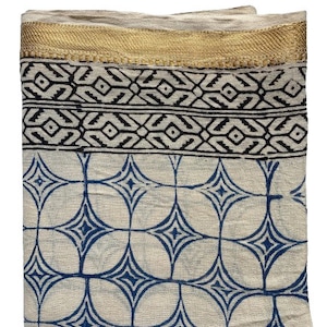 May include: A white cotton scarf with a blue and white geometric pattern. The scarf has a gold trim around the edges.