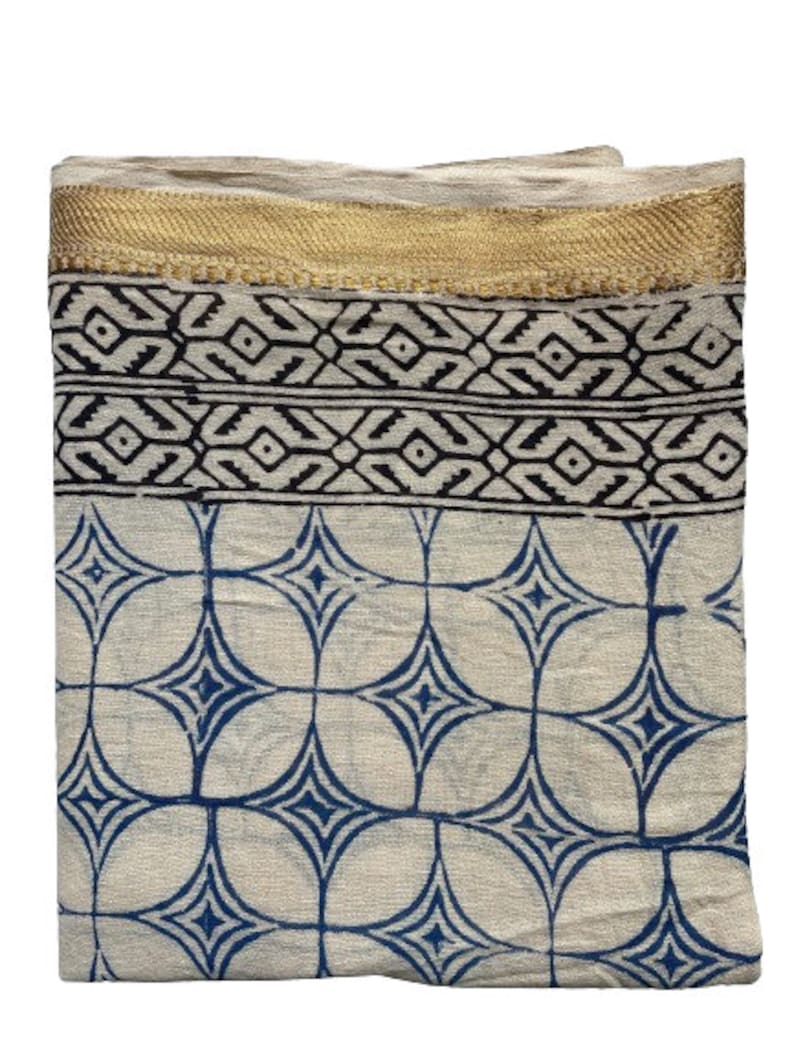 May include: A white cotton scarf with a blue and white geometric pattern. The scarf has a gold trim around the edges.