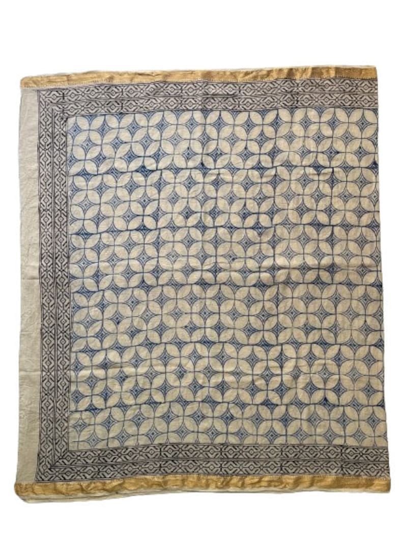 May include: A white cotton fabric with a blue and white geometric pattern. The fabric has a gold border.