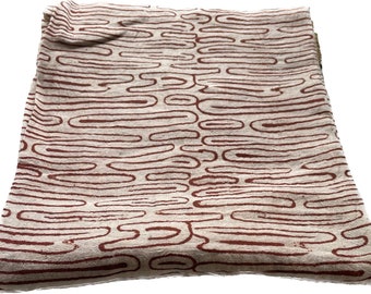 May include: Folded fabric with a repeating pattern of dark red, wavy lines on a light beige background. The fabric appears to be soft and possibly linen or cotton, with a slightly textured surface.