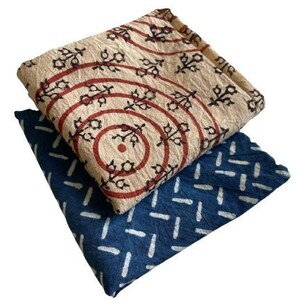 May include: Two fabric squares with different patterns. The top square is beige with red and black circles and floral designs. The bottom square is blue with white stripes.