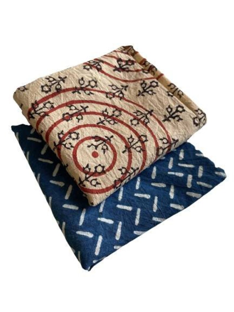 May include: Two fabric squares with different patterns. The top square is beige with red and black circles and floral designs. The bottom square is blue with white stripes.