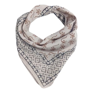 May include: Cream-colored bandana with brown floral and geometric patterns. The bandana is folded into a triangle shape, with a detailed border design in black. The overall design is symmetrical and the fabric appears soft.