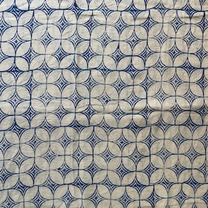 May include: A white fabric with a repeating blue geometric pattern. The pattern is made up of overlapping circles and stars.