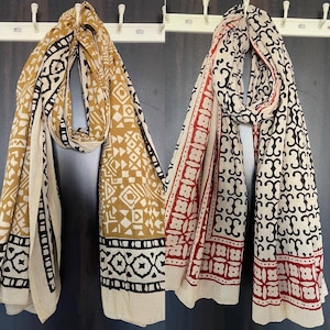 May include: Two cotton scarves with block printed designs. One scarf is beige with black and mustard yellow geometric patterns. The other scarf is beige with black and red geometric patterns.
