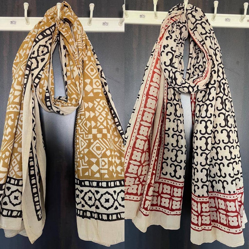 May include: Two cotton scarves with block printed designs. One scarf is beige with black and mustard yellow geometric patterns. The other scarf is beige with black and red geometric patterns.