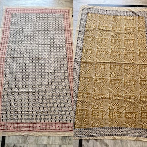 May include: Two fabric squares with different patterns. The square on the left has a black and white geometric pattern with a red and white border. The square on the right has a brown and white geometric pattern with a black and white border.