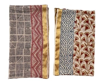 May include: Two folded fabric pieces with block print patterns. One features a grid and geometric design in black and red on a cream background, with a gold border. The other has a floral and geometric pattern in blue and brown.