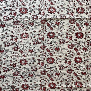 May include: White fabric with a repeating pattern of red and black floral designs.