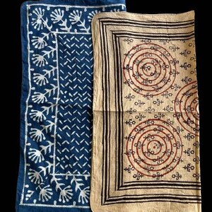 May include: Two fabric squares with different patterns. The square on the left is blue with a white floral design. The square on the right is beige with a brown and red circular pattern.