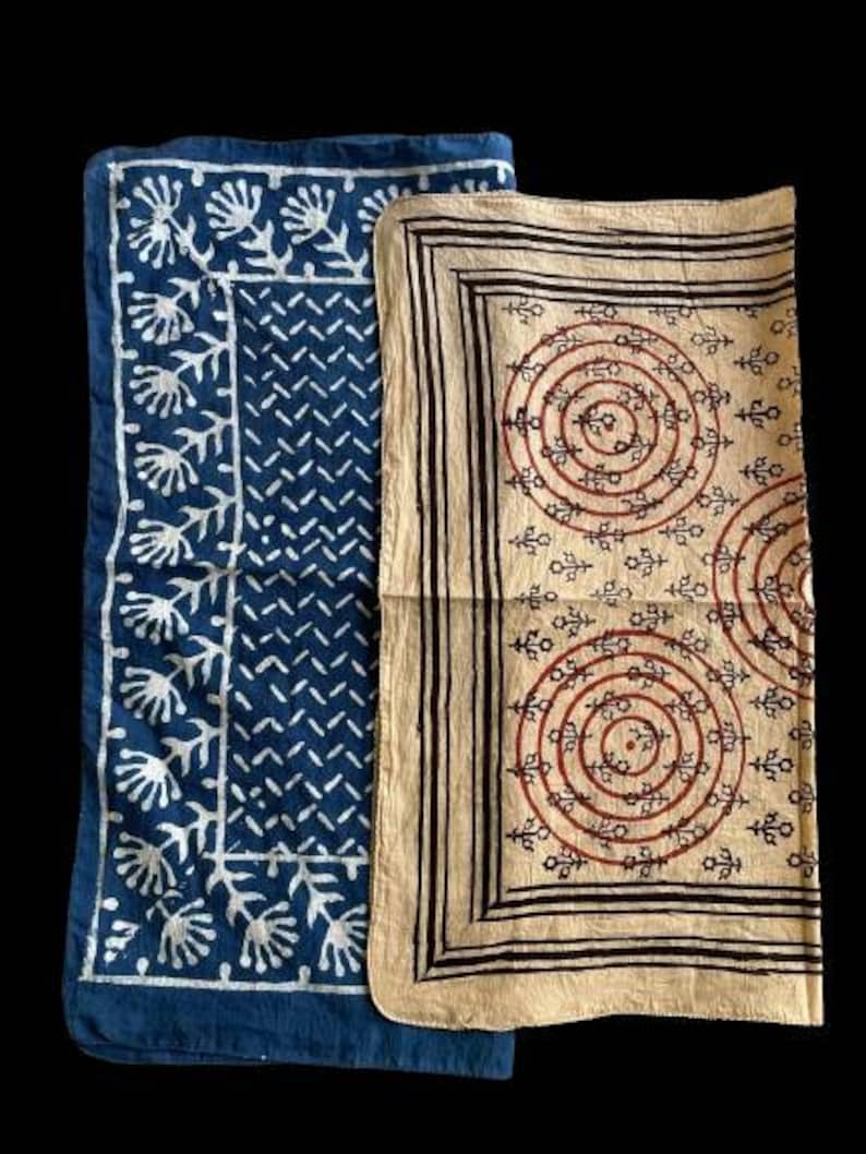 May include: Two fabric squares with different patterns. The square on the left is blue with a white floral design. The square on the right is beige with a brown and red circular pattern.