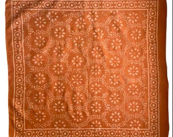 May include: A square orange bandana with a white floral pattern and a white border. The bandana is made of cotton and has a soft, comfortable feel.