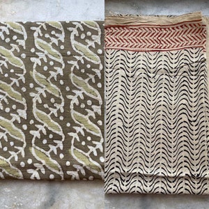 May include: Two fabric pieces with distinct patterns. One features a repeating design of stylized birds and leaves in olive green and light green on a darker olive background. The other has a cream base with black wavy lines and a red and cream border.